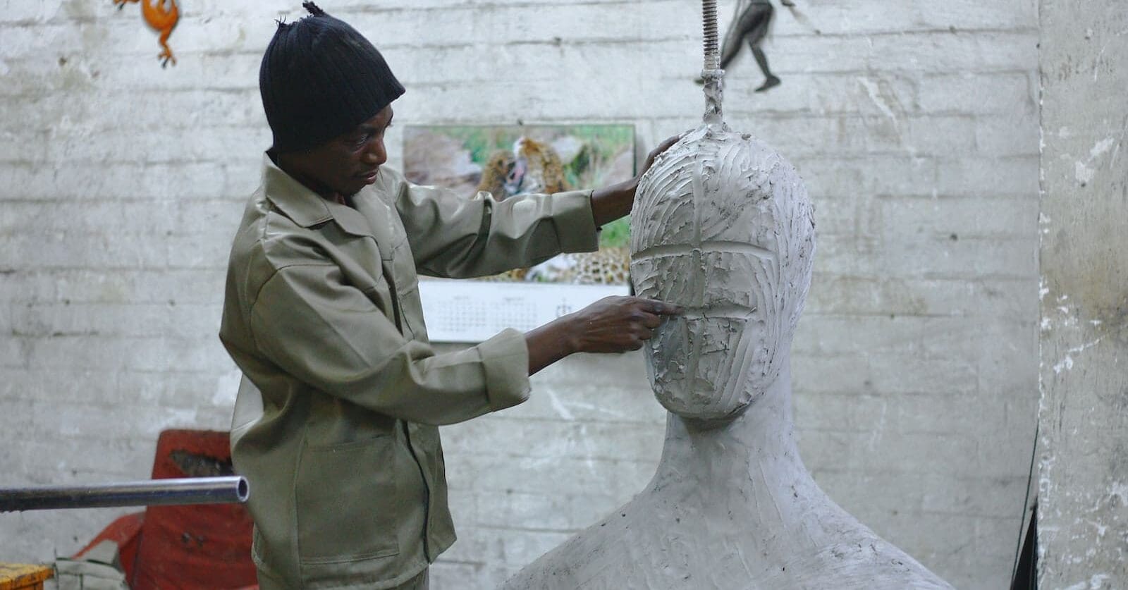 A sculptor works in his studio sculpting a large white body and head. He is a creator