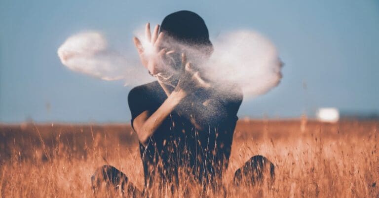 man sitting on brown grass field playing with smoke like a magician