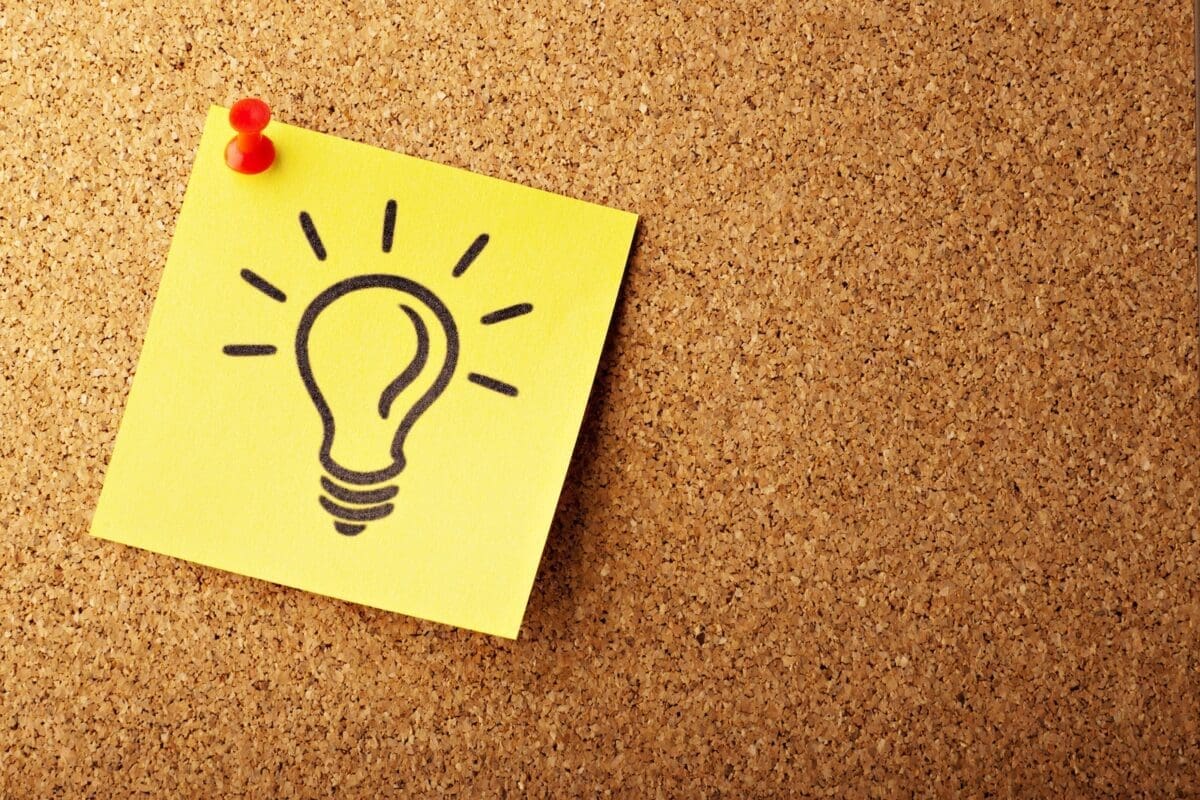 yellow post-it with the image of a bulb on it, pinned to a cork board with a red pin