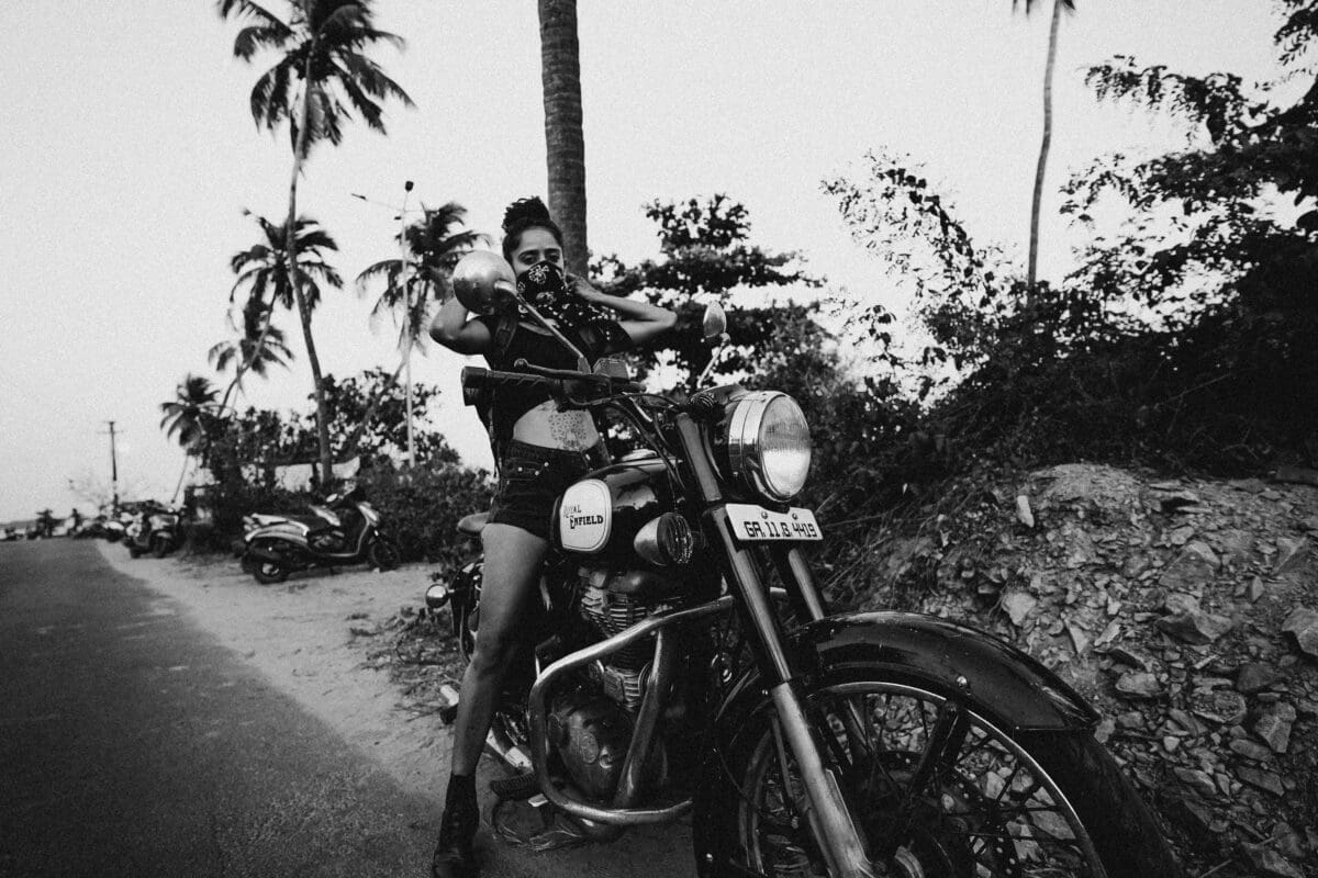 Black and White image of a Woman on a royal Enfield bike, representing an outlaw or rebel
