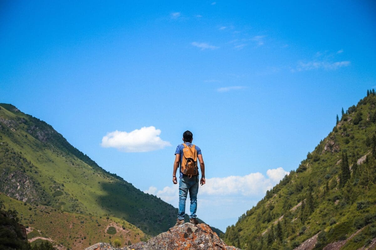 Man with backpack standing on a cliff, looking at mountains, indicating an explorer
