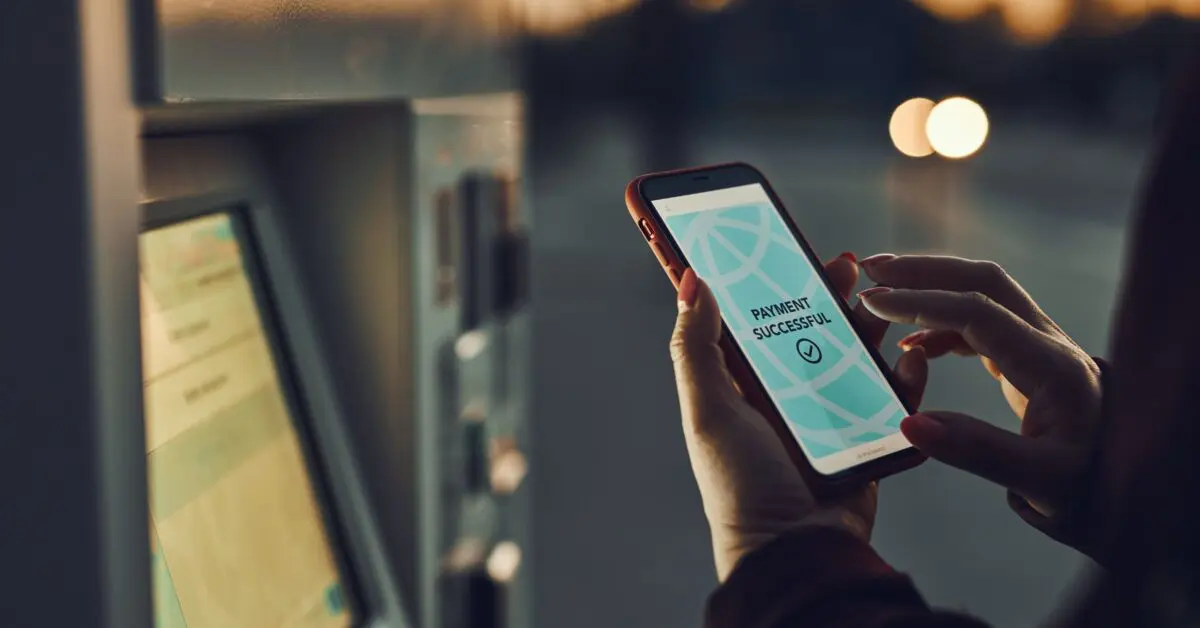 A person holding a smartphone near a ticketing machine. The screen on the phone reads "PAYMENT SUCCESSFUL". The image emphasizes the convenience, speed, and security of payments made using RAG technology.